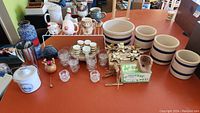 Top down photo of lot items on orange table: crocks, glasses, candle holders, and other items