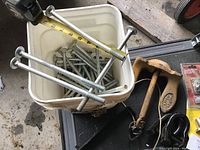 Bucket of galvanized hex bolts with measuring tape showing bolt length near 7 inches