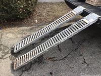 Top view of the pair of two metal loading ramps shown outdoors on pavement with visible rust.