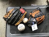 Overview photo showing both Rawlings and Adidas left-handed baseball gloves with two softballs on a gray surface.