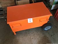 Closed view of the orange metal battery lock box showing rectangular shape, wheels, and side handles.