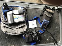 All three cameras including Sony Digital Mavica MVC-FD73, Nikon N2000 SLR, Canon PowerShot SD1300 IS digital camera along with a carrying bag and Nikon strap on dark floor