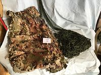Two green army-style hammocks with bundled dark green camouflage net on white backdrop.