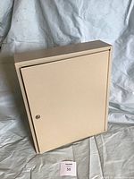 Closed beige metal key storage cabinet showing front door with lock and flat top surface.