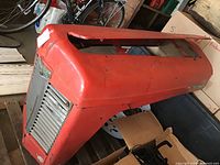 Side angle of red Massey Ferguson tractor hood showing grills and badge with some wear and scratches