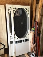 Full view of white PVC screen door leaning against a wall, showing decorative scrollwork and mesh screen.