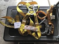 Yellow Durabilit safety harness with metal D-ring and attached Titan orange shock absorbing lanyard on black container