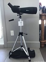 Full view of spotting scope mounted on tripod with carrying case on floor beneath