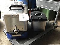 Two T-fal oil fryers side by side on a metal surface.