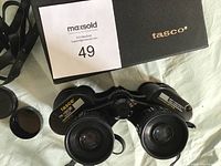Tasco 15x35 binoculars and black Tasco carrying case with MaxSold auction card on white fabric background.