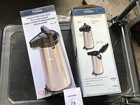 Two boxed Trudeau stainless steel pump carafes showing product name, capacity, and features including glass vacuum insulation and pump lid.