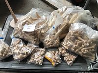 Large lot of multiple bags containing turned wooden pegs and finials arranged on a metal cart, showing various shapes and sizes clearly visible through packaging.