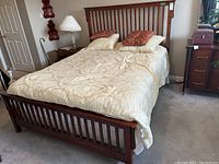 Full view of queen wooden bed with cream damask duvet and pillows on a carpeted floor.