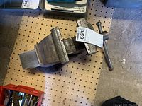 Overview showing the full heavy bench vice made of cast metal with a screw handle and flat jaws, placed on a perforated surface.