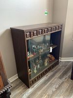 View of the cabinet angled to show carved wood panel details and sliding glass doors with displayed figurines inside