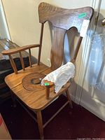 Full view of the vintage wood commode chair showing high back, armrests, and seat cover with lace cloth on one armrest.