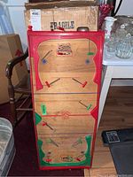 Wood hockey game with red frame, colored pegs on rods for players, original box behind.