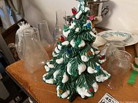 Front view of ceramic Christmas tree with glass chimneys arranged behind it.