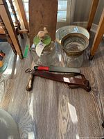 Photo of jars with green lid and carved bird top, sharpening stone with red and black handle, butcher's saw frame with leather sheath, white bowl containing smaller glass jars.