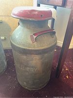 Full view of the metal milk jug with red lid, showing embossed company name 'Creamery'.