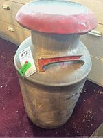 Full front view of the vintage metal milk jug showing embossed letterings and red lid rim.