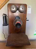 Frontal view of the wooden wall-mounted Kellogg Switchboard Supply Co. phone with two metal bells and attached black earpiece.