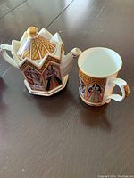 Photo of Sadler teapot and matching mug on wooden surface showing side panels with portraits of King Henry VIII and each of his six wives.