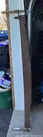 Full length of the antique two-man saw showing the blade and one wooden handle leaning against a wall near a garage.