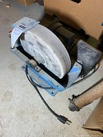 Front and side view of the grinding wheel with power cord visible and attached to the blue metal base.