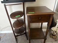 Two wooden side tables shown side by side, one rectangular with drawer and turned legs; other is round tiered stand with damage visible on the top tier.