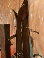 Side view of a pair of vintage wooden skis with curved tips and attached bindings.