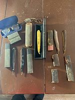 Overview of the lot on a wooden surface showing six straight razors, their cases, and two pairs of vintage eyeglasses with cases.