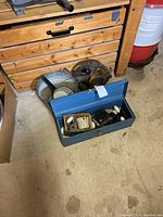 Metal toolbox containing assorted door hardware alongside rope maker and bucket.