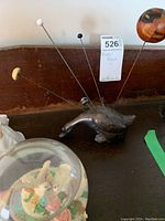 Photo of metal hat pin holder shaped like an animal with several hat pins inserted, including one with a pumpkin design.