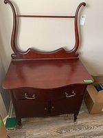Full view of the wooden wash stand showing the bull's horn side supports, drawer with brass handles, cabinet doors, and castors.