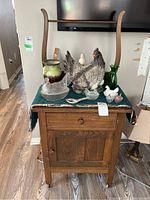 Front view of wood wash stand with drawer and cabinet, covered top with decorative cloth and various ceramic items on top.