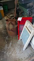 Photo showing vintage metal watering can with handle and spout next to two wooden washboards in a garage setting