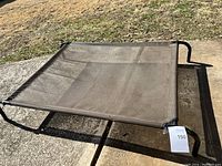 Side angle view showing the structure and mesh fabric of the elevated dog bed outdoors on a concrete surface.