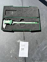Electronic caliper gauge in open green plastic foam-lined carrying case with Allen wrench inserted.