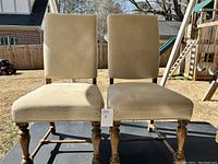 Front view of two beige fabric Haverty's dining chairs showing overall fabric stains and wooden legs with carved details.