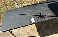 Full view of the fishing rod and attached reel laying on a black table outdoors.