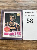 Kareem Abdul-Jabbar basketball card sleeved and next to a lot number card on a wood floor.