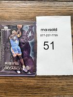 Photo of Kobe Bryant basketball card in protective sleeve with lot number 51 in background.