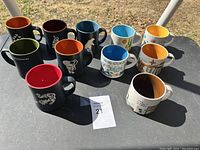 Photo showing all eleven limited edition Starbucks mugs arranged on a table with various colored interiors and designs.