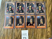 Eight Kobe Bryant basketball cards arranged in two rows of four on wood floor, all in protective sleeves showing the front faces.
