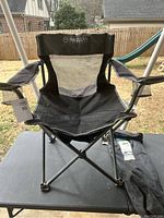 Front view of black Magellan Outdoors folding chair showing armrests and fabric seat structure on outdoor table.