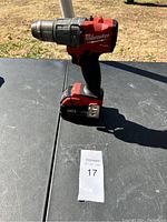 Full view of Milwaukee cordless hammer drill on black surface outdoors with sunlight.