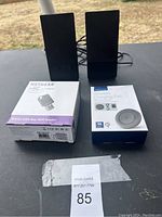 Two Sony VAIO black speakers, Insignia wireless charging pad boxed, Netgear wireless adapter boxed on a black surface outside