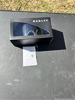 Photo of Oakley goggles black box showing lens through window with outdoor background.
