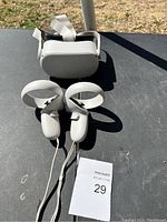 Oculus VR headset and two white controllers arranged on a table under sunlight showing overall condition and setup.